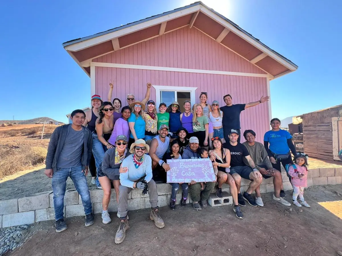 Volunteers and a family in front of the pink home they built together in Mexico, holding a Bienvenidos a Casa sign